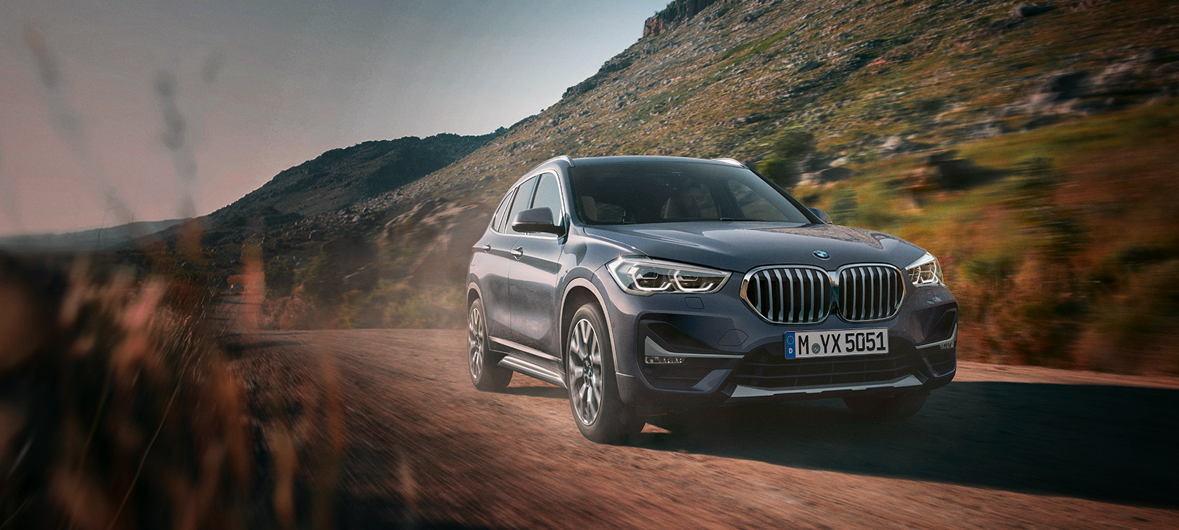 BMW X1 F48 LCI Storm Bay three-quarter front view driving in front of mountain scenery